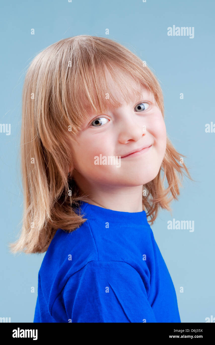 Studio Portrait Of A Boy With Long Blond Hair Isolated On Blue