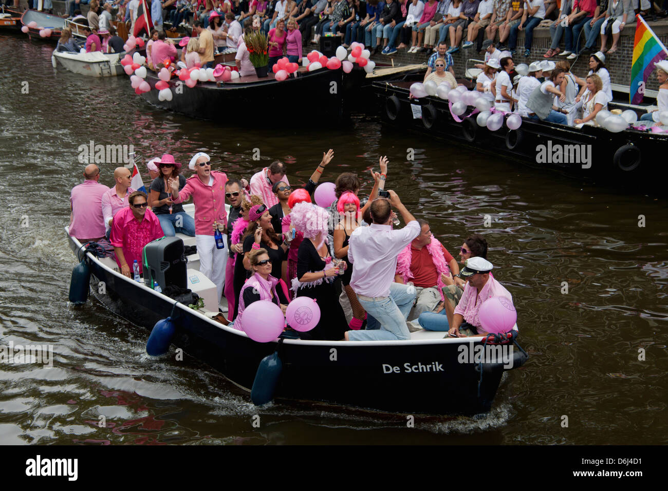 The Gay Pride Parade Down A Crowded Canal Lined With People And Boats In Amsterdam Holland