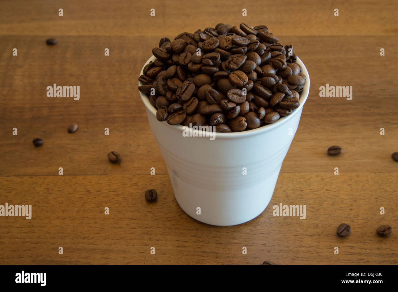 A white coffee cup filled with coffee beans. It is depicting peoples excessive intake of coffee but at the same time enticing. Stock Photo