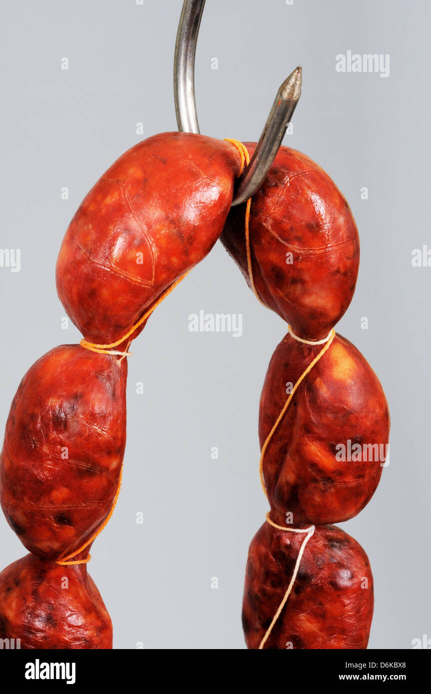 String of Spanish Chorizo sausage hanging from a meat hook against a grey background. Stock Photo