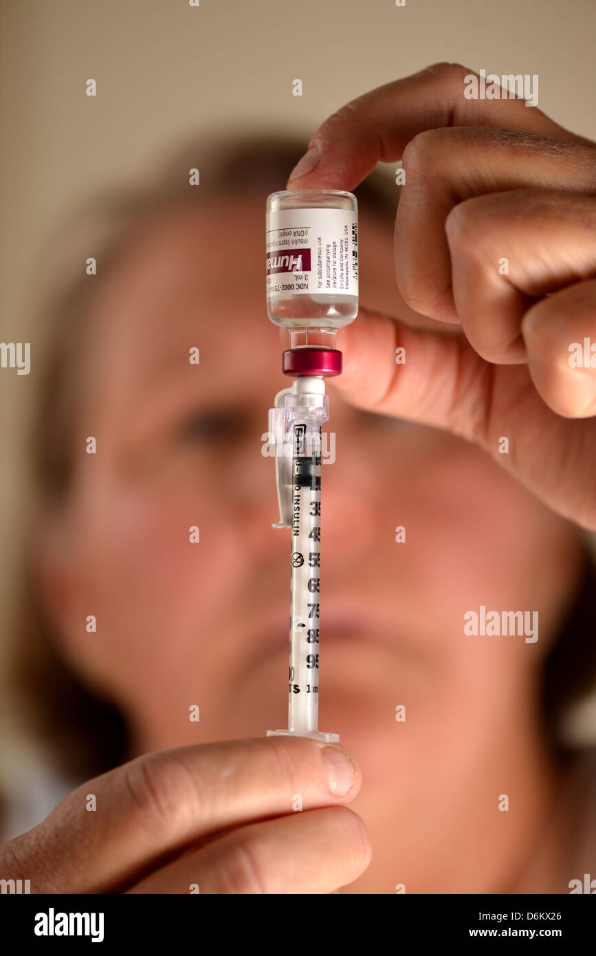 A senior female prepares a syringe with insulin, which is used to treat