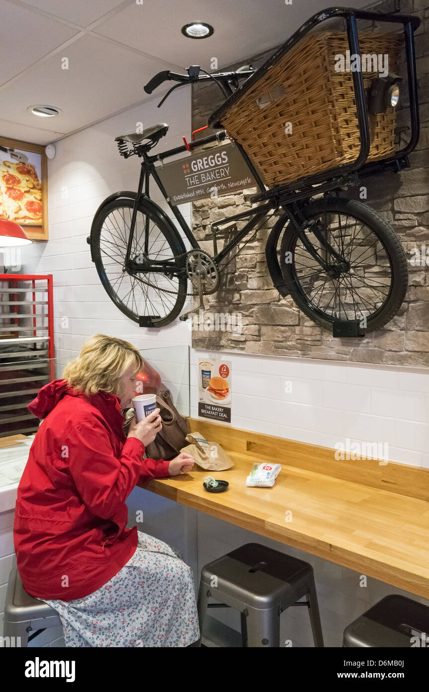 Woman sitting inside Greggs Gosforth shop drinking tea north east England UK Stock Photo