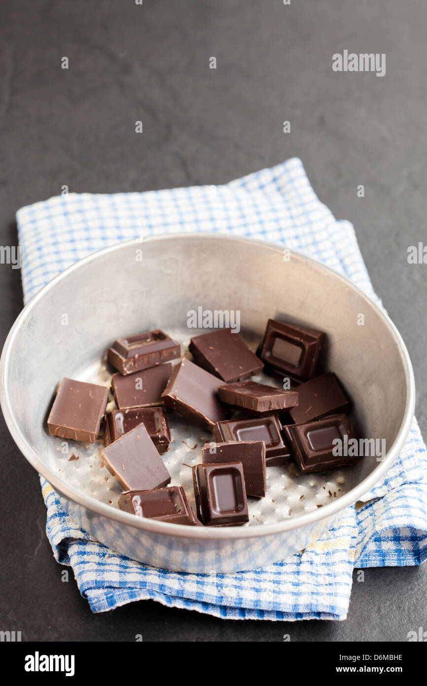 Closeup of bowl containing pieces of chocolate resting on blue checkered napkin on dark background Stock Photo
