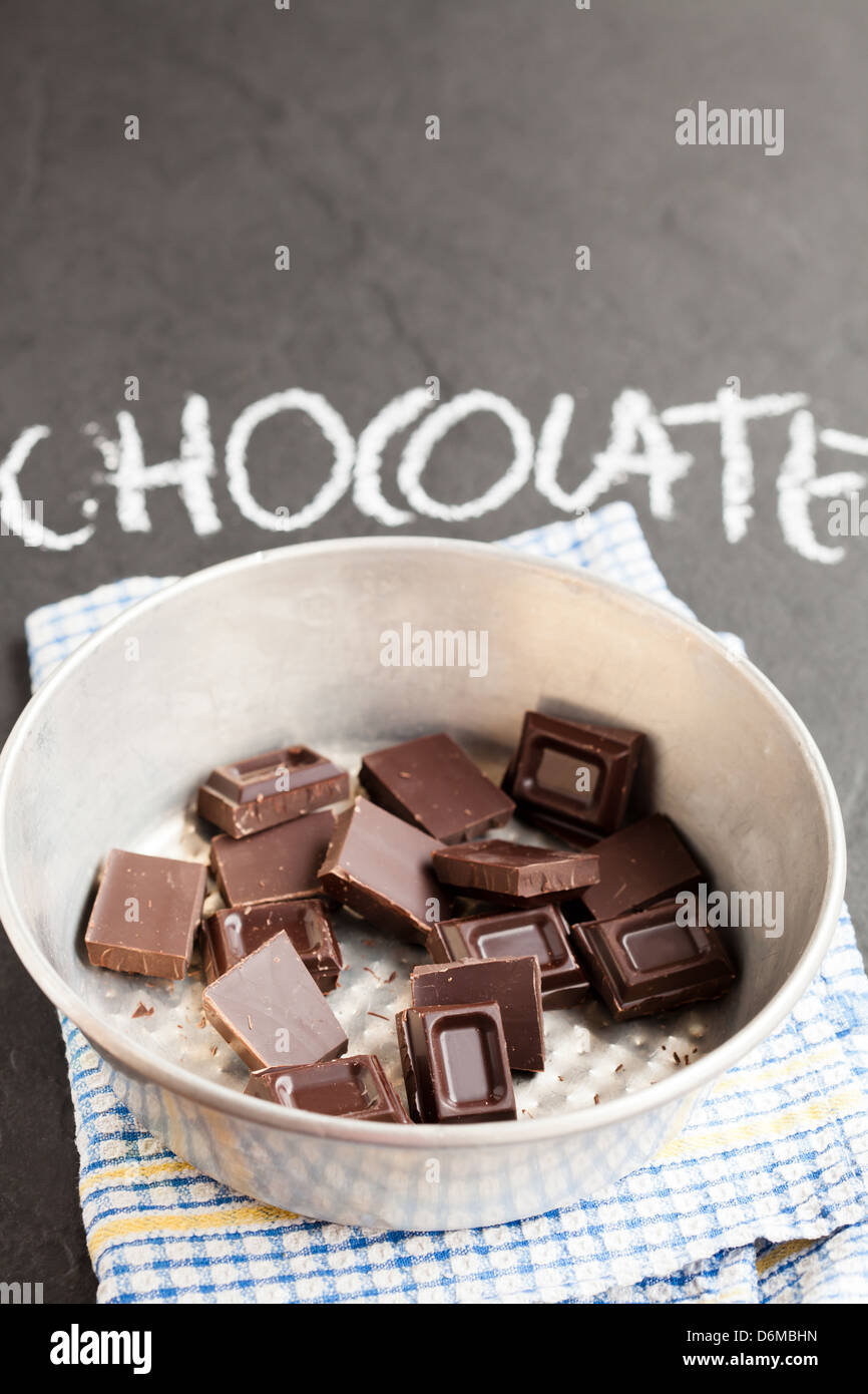 Bowl containing chocolate squares with word chocolate written in chalk on dark background Stock Photo