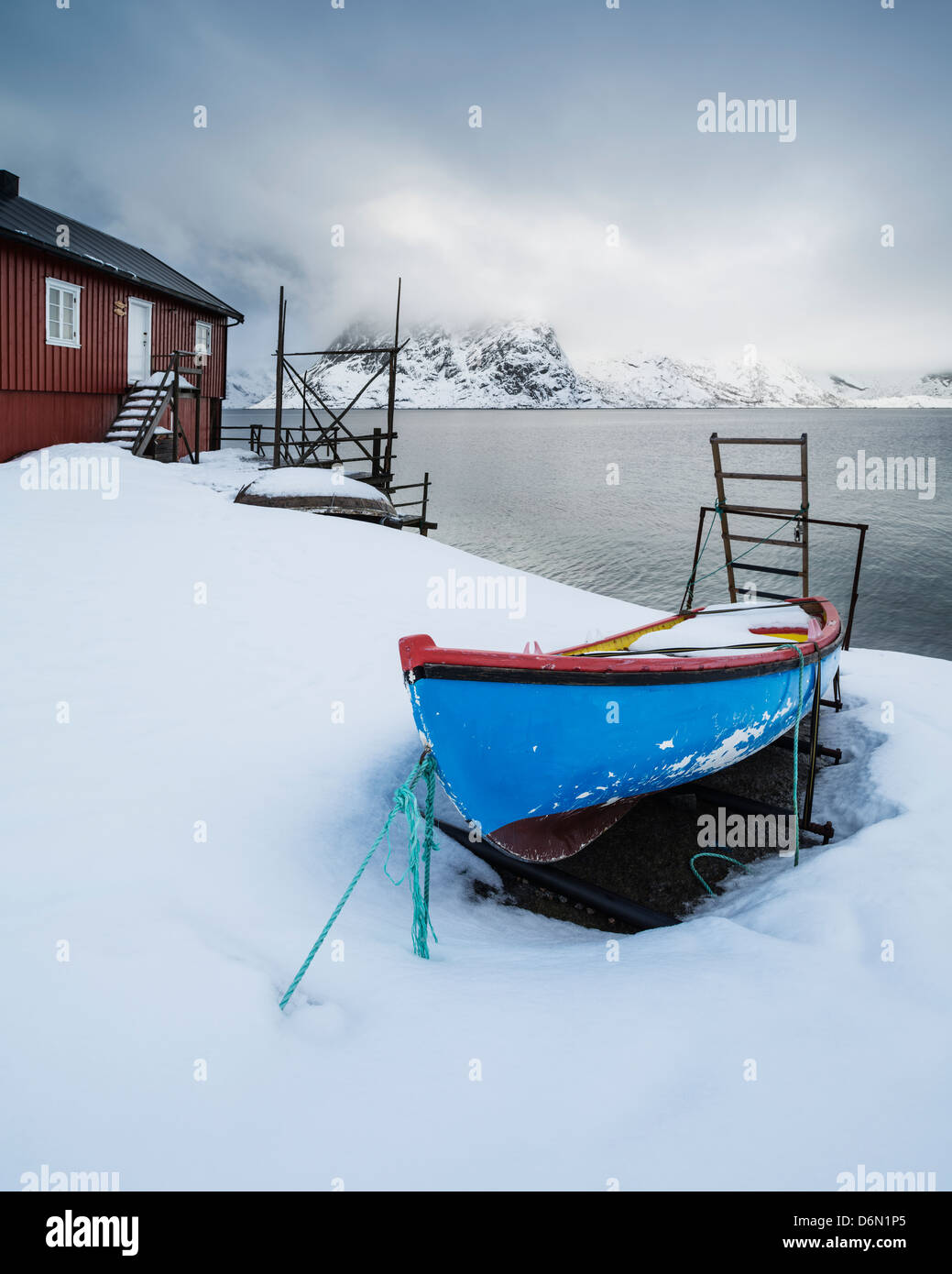 Small row boat surrounded by snow outside traditional Rorbu cabin, Toppøya, Moskenesøy, Lofoten Islands, Norway Stock Photo
