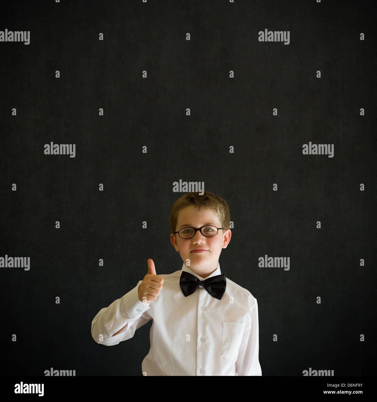 Thumbs up sign boy dressed up as business man, teacher or student on blackboard background Stock Photo