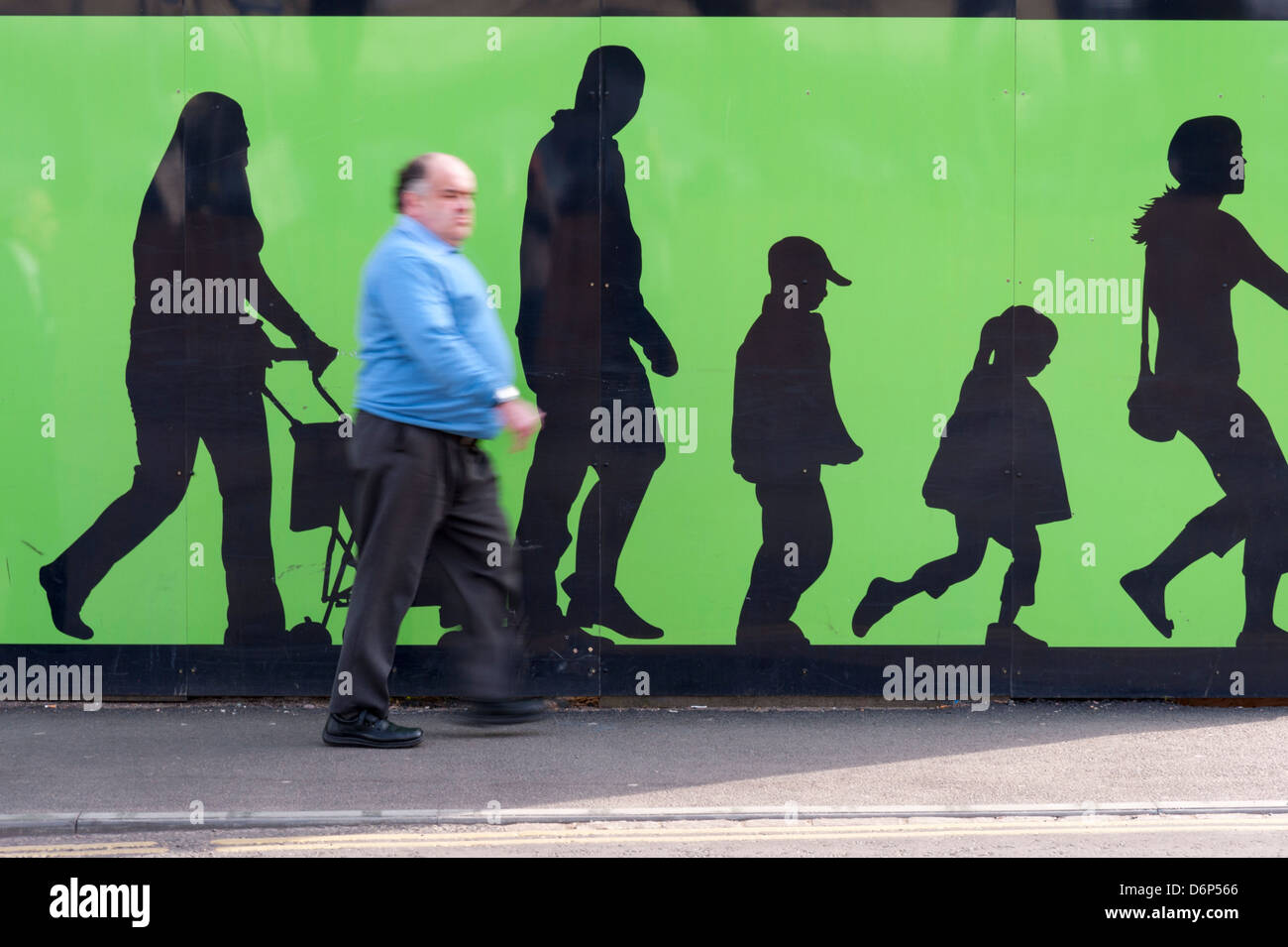 Real people walking in front of a city mural which has painted silhouettes of people walking in the background in Cambridge UK Stock Photo