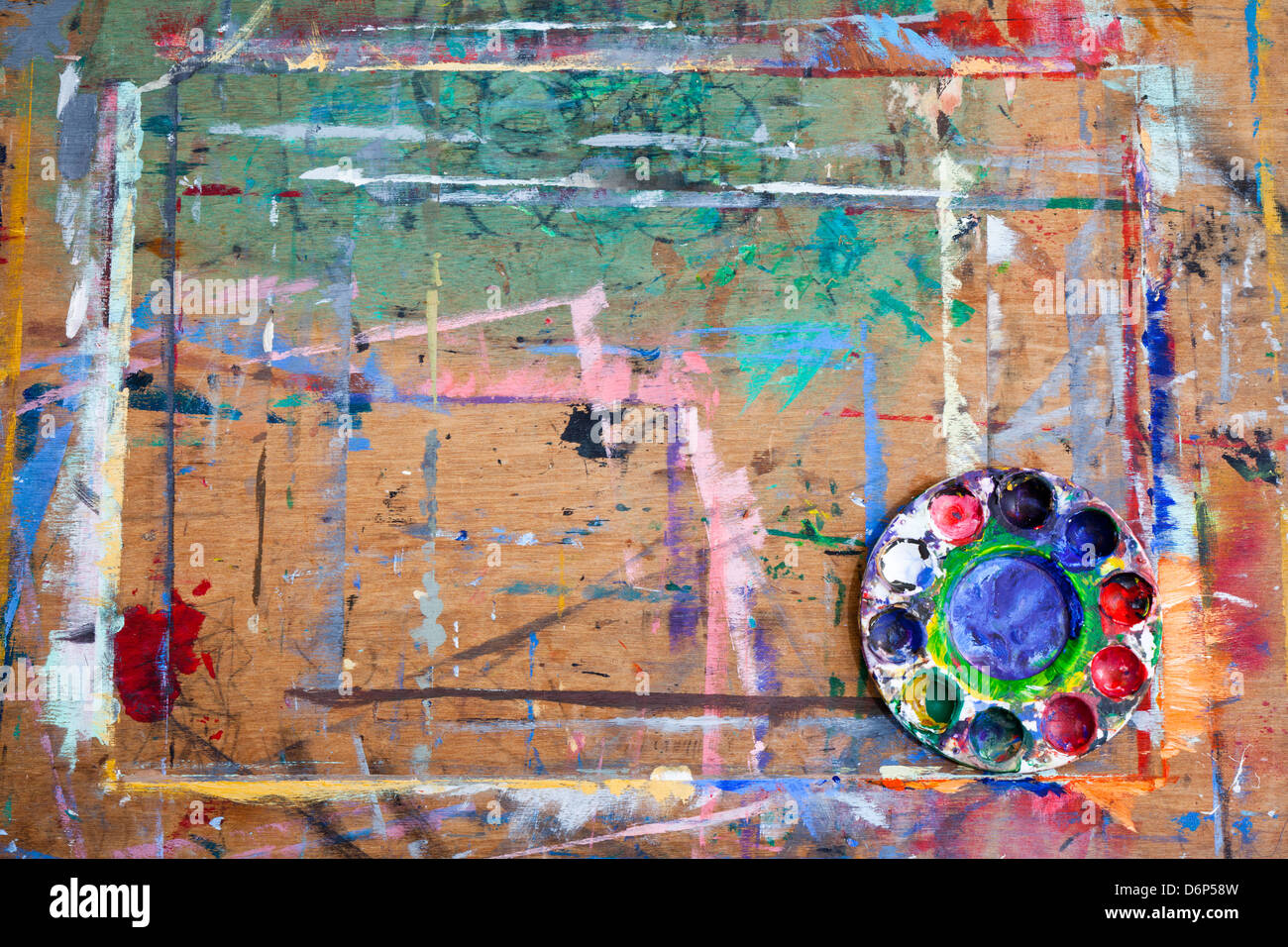A paint splashed wooden board with a messy plastic paint palette in the