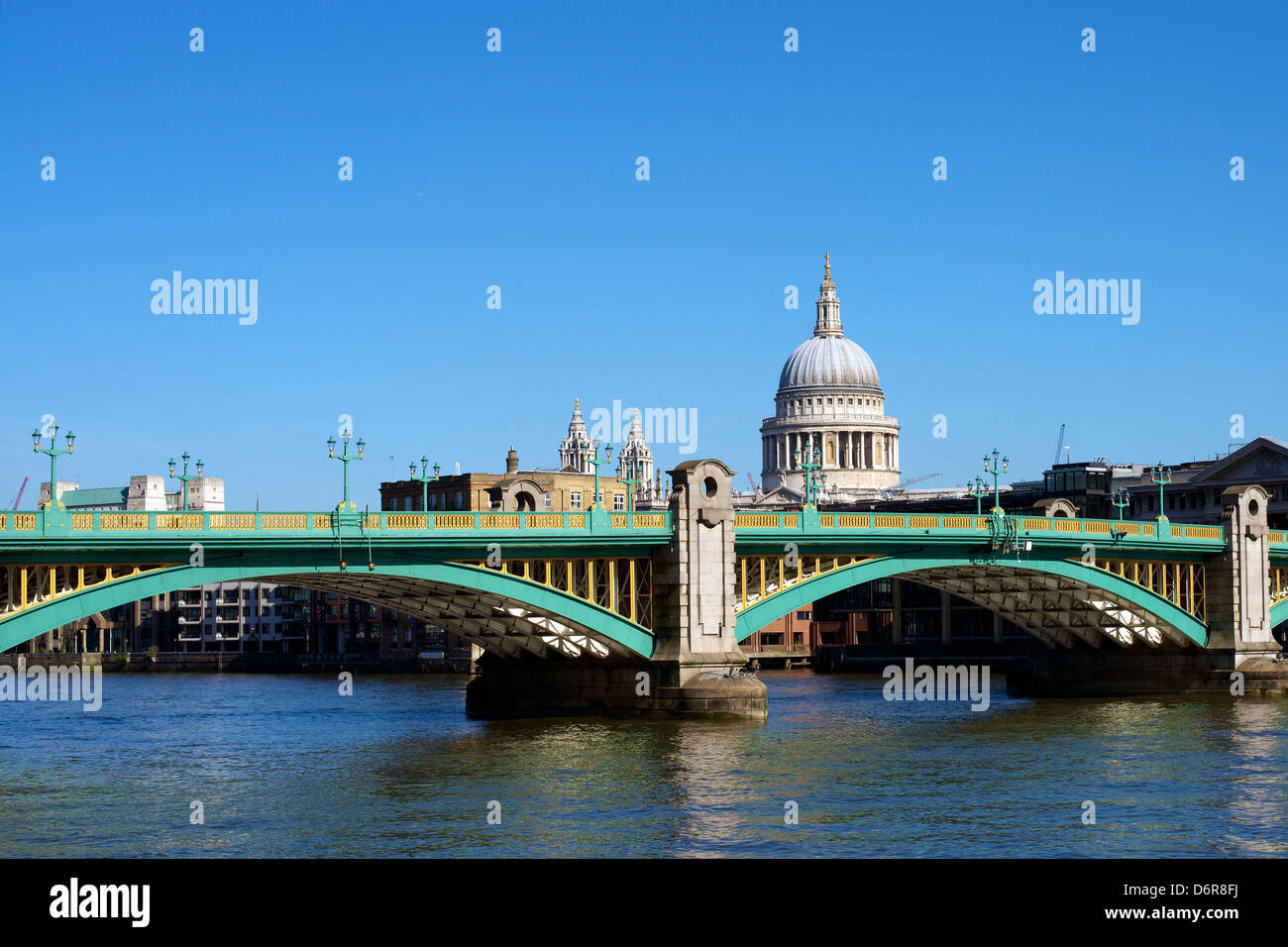 Pillars supports and arches of Southwark Bridge in London set against a clear blue sky with St Paul's Cathedral in the distance Stock Photo