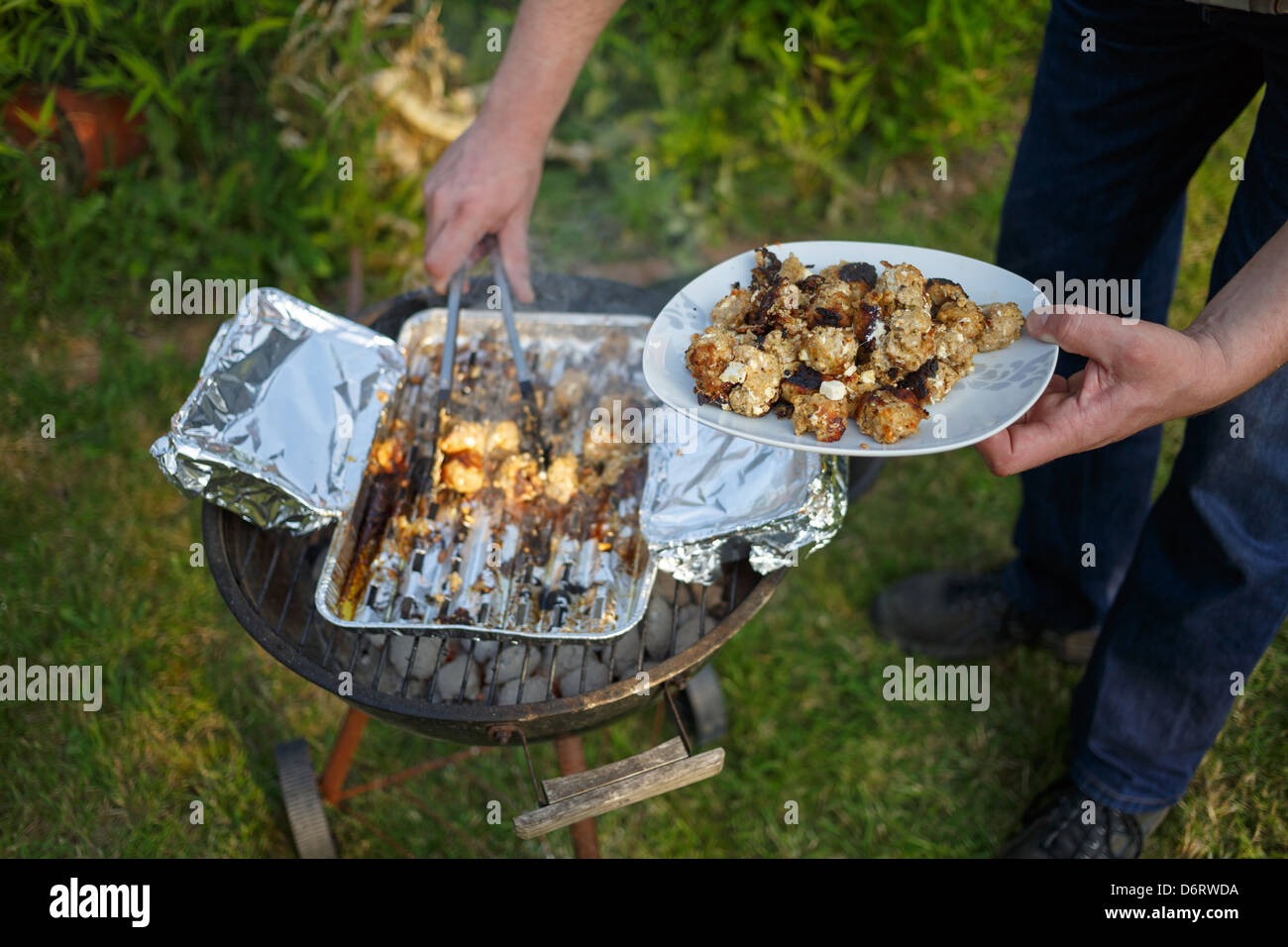 Emden, Germany, a man takes with barbecue tongs Hackbaellchen from an aluminum shell of a charcoal grill Stock Photo