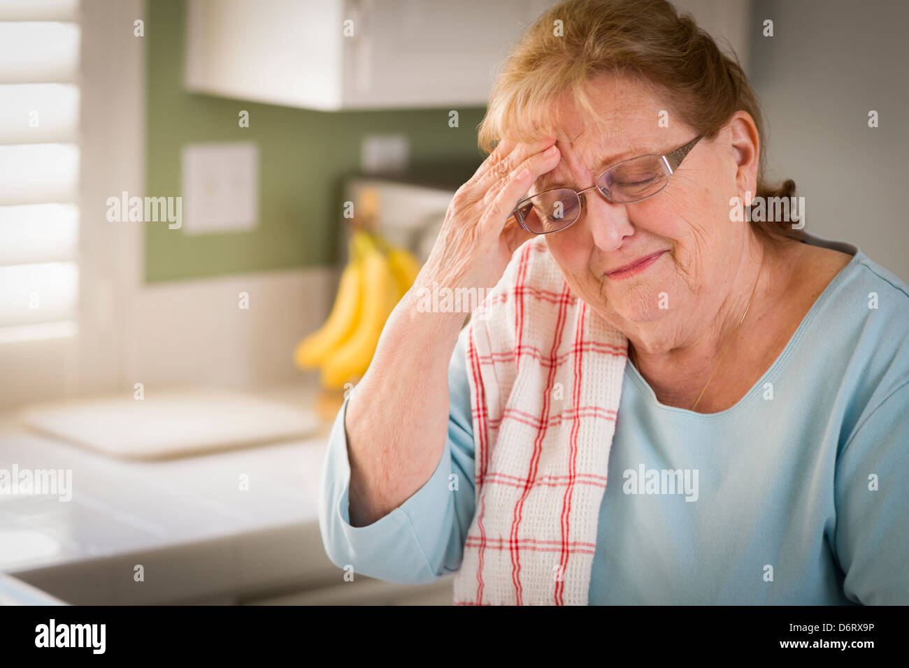 Sad Crying Senior Adult Woman At Kitchen Sink in Home. Stock Photo