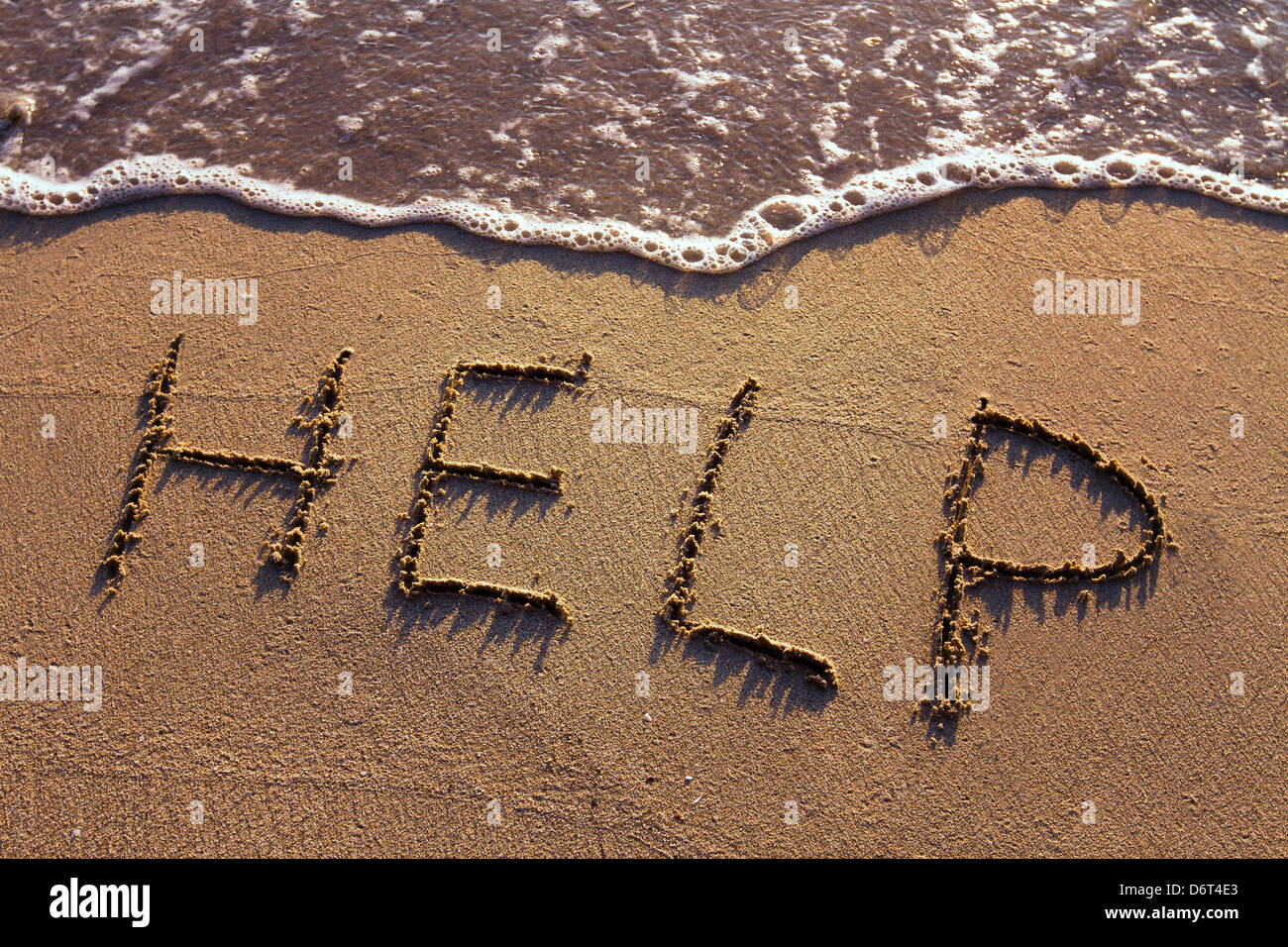 word HELP handwritten on the sand Stock Photo