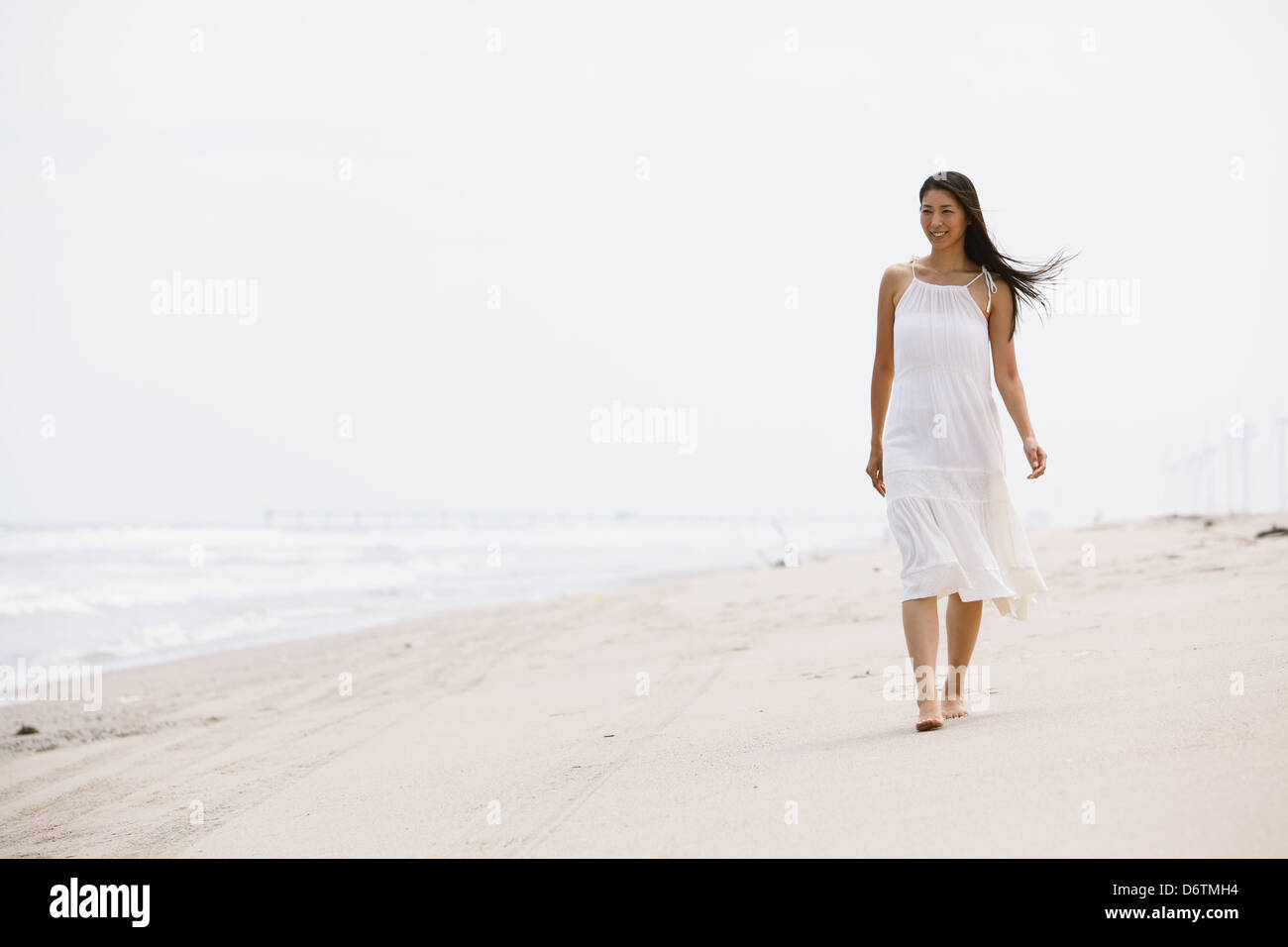 Woman in a white dress walking on the beach Stock Photo - Alamy