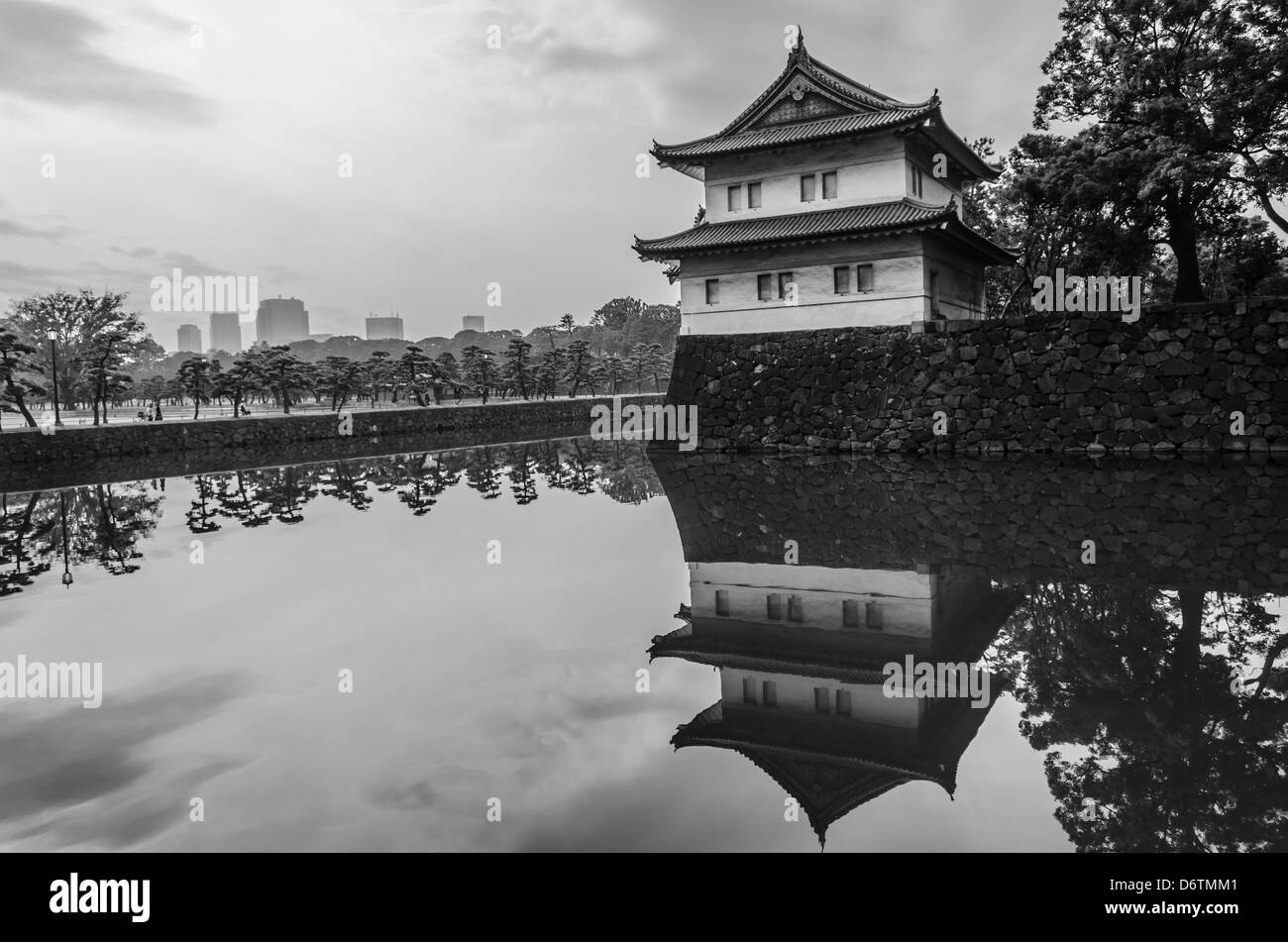 Black and white of part of Edo Castle in Tokyo, Japan with surrounding moat in foreground and trees, skyscrapers in background Stock Photo