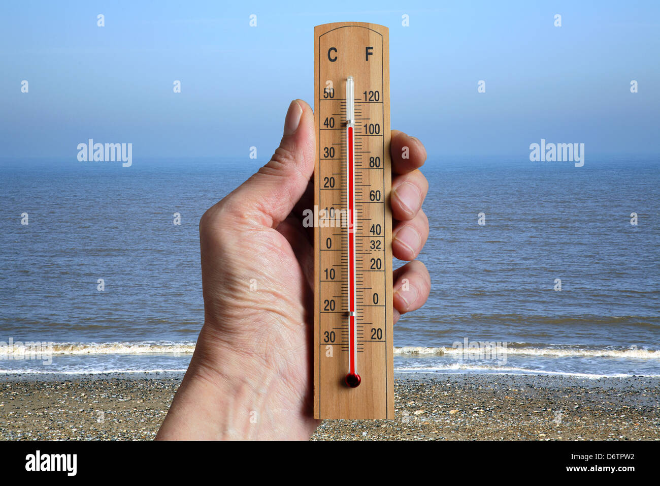 Hand holding a thermometer indicating climate change due to increasing global temperatures. Stock Photo
