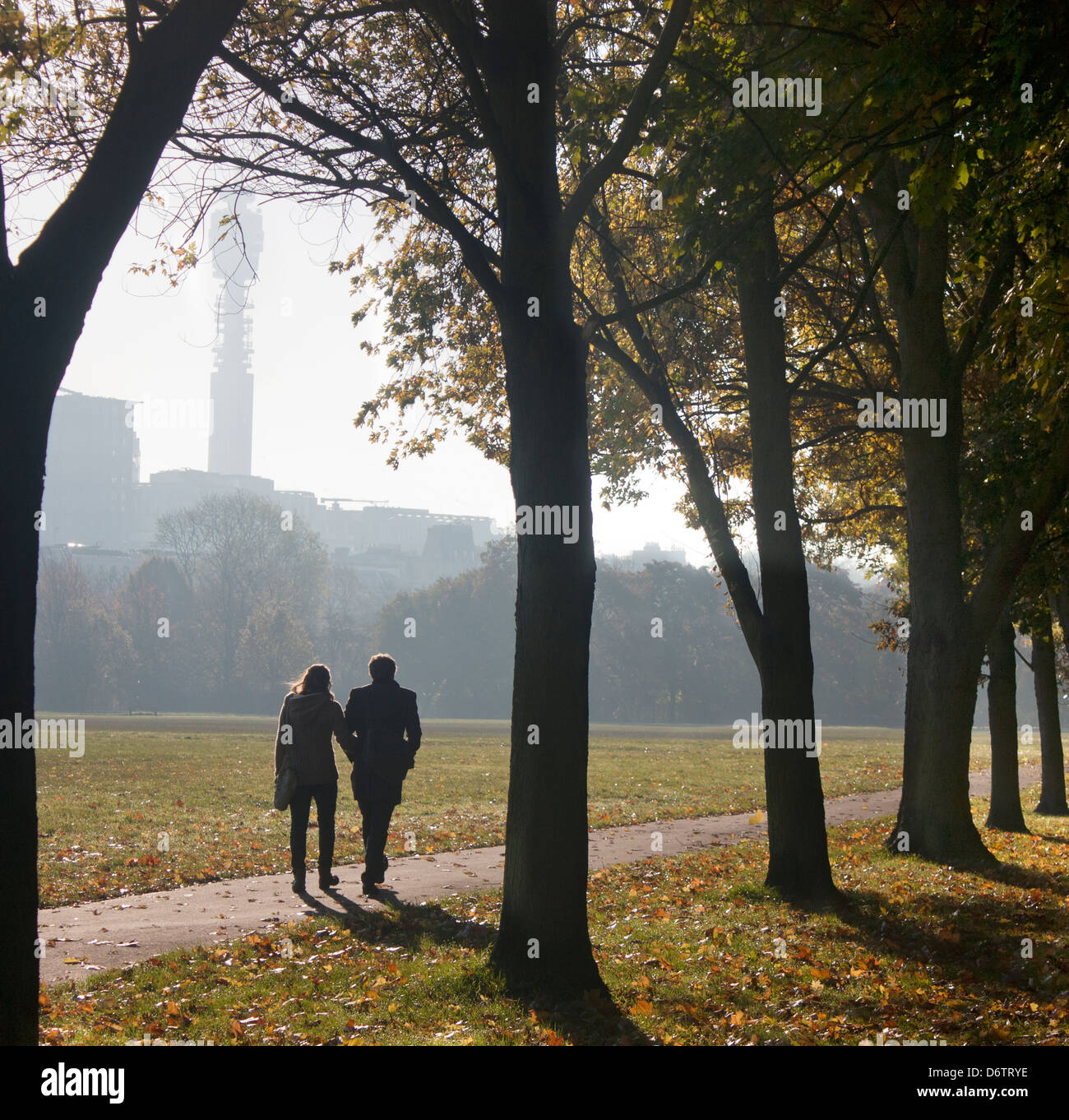 Couple walking through The Regent's Park in early autumn morning with BT Tower in silhouette in distance London England UK Stock Photo