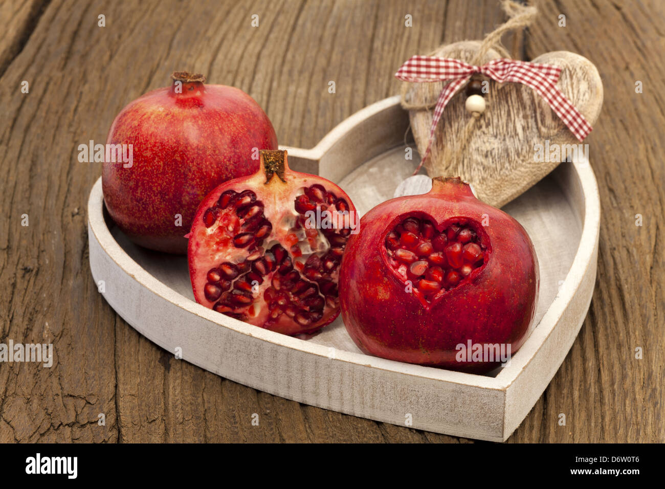 Two whole and one half pomegranate on a tray with a wooden heart, a pomegranate with a heart-shaped cutout Stock Photo