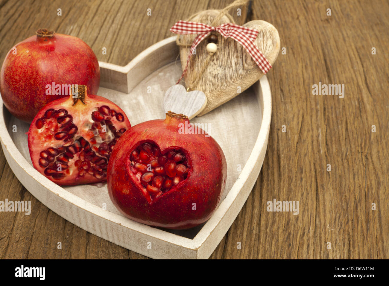 Two whole and one half pomegranate on a tray with a wooden heart, a pomegranate with a heart-shaped cutout Stock Photo