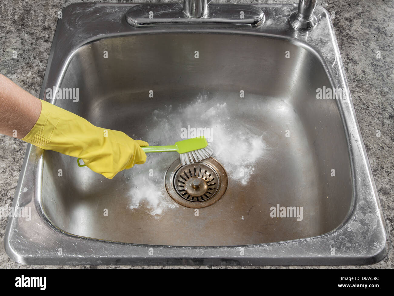 Female hand in yellow glove cleaning the kitchen sink. Stock Photo