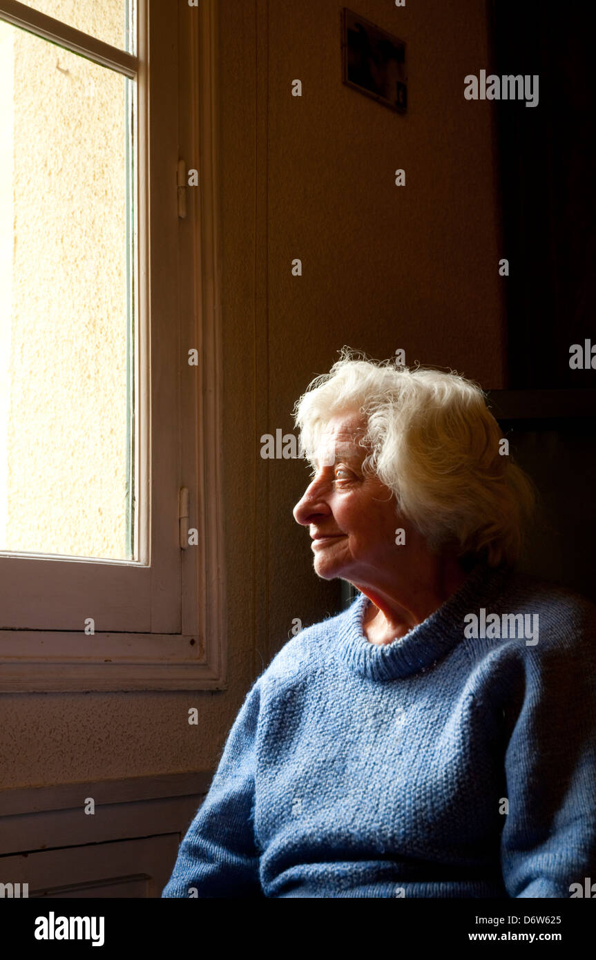 Portrait of old woman at home, smiling and looking at the window. Stock Photo