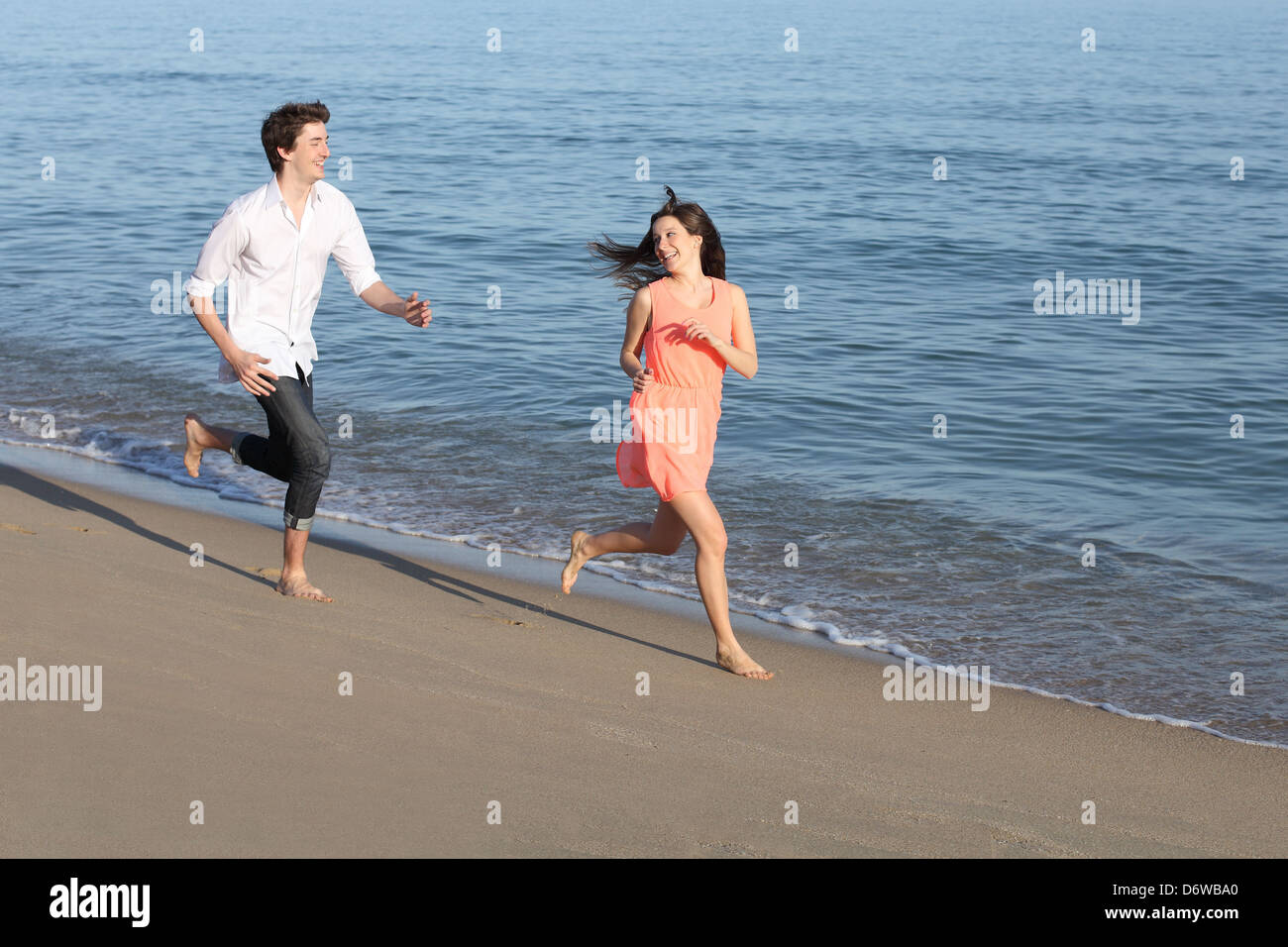 Couple of teenagers running and flirting on the beach shore near the water Stock Photo