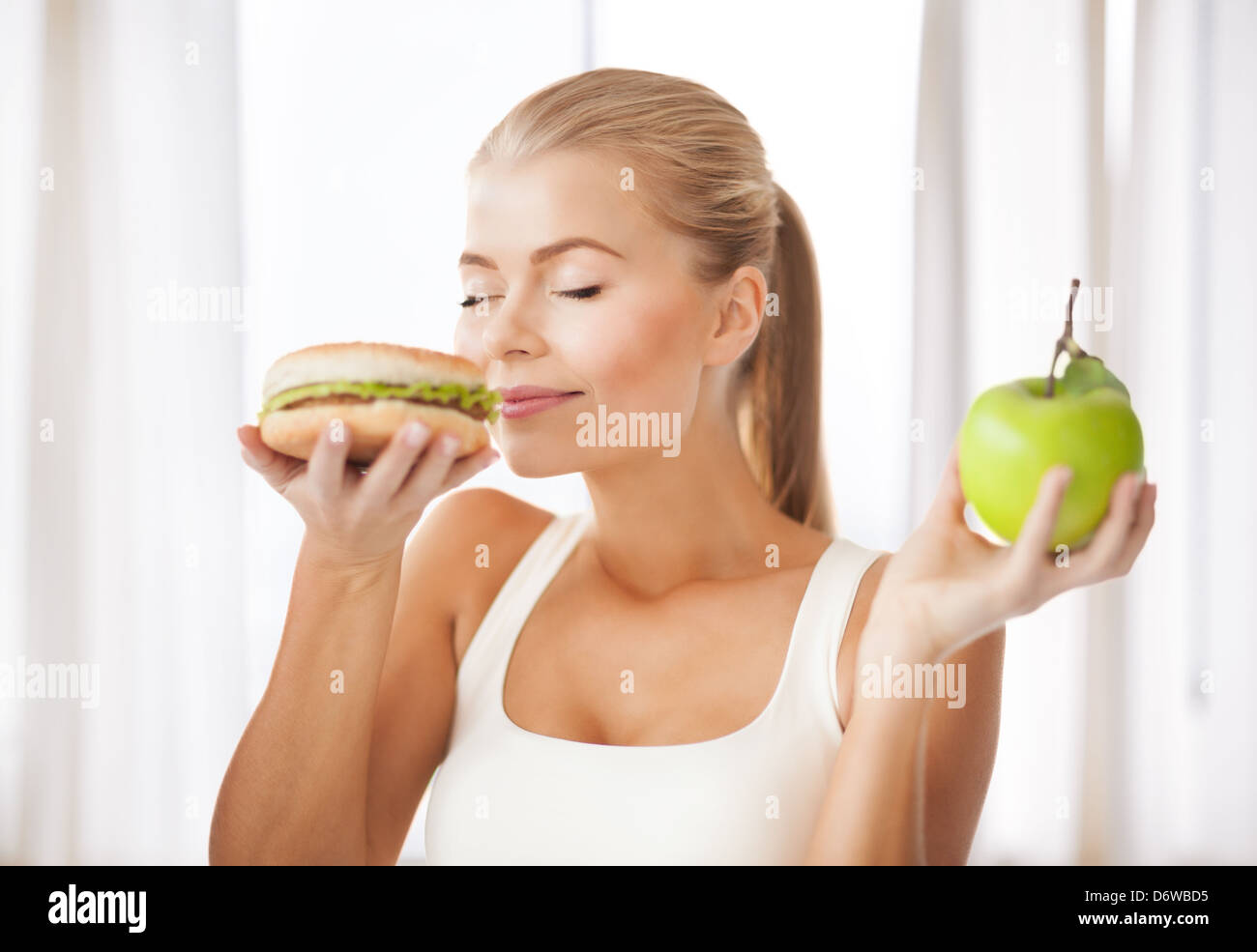 woman smelling hamburger and holding apple Stock Photo