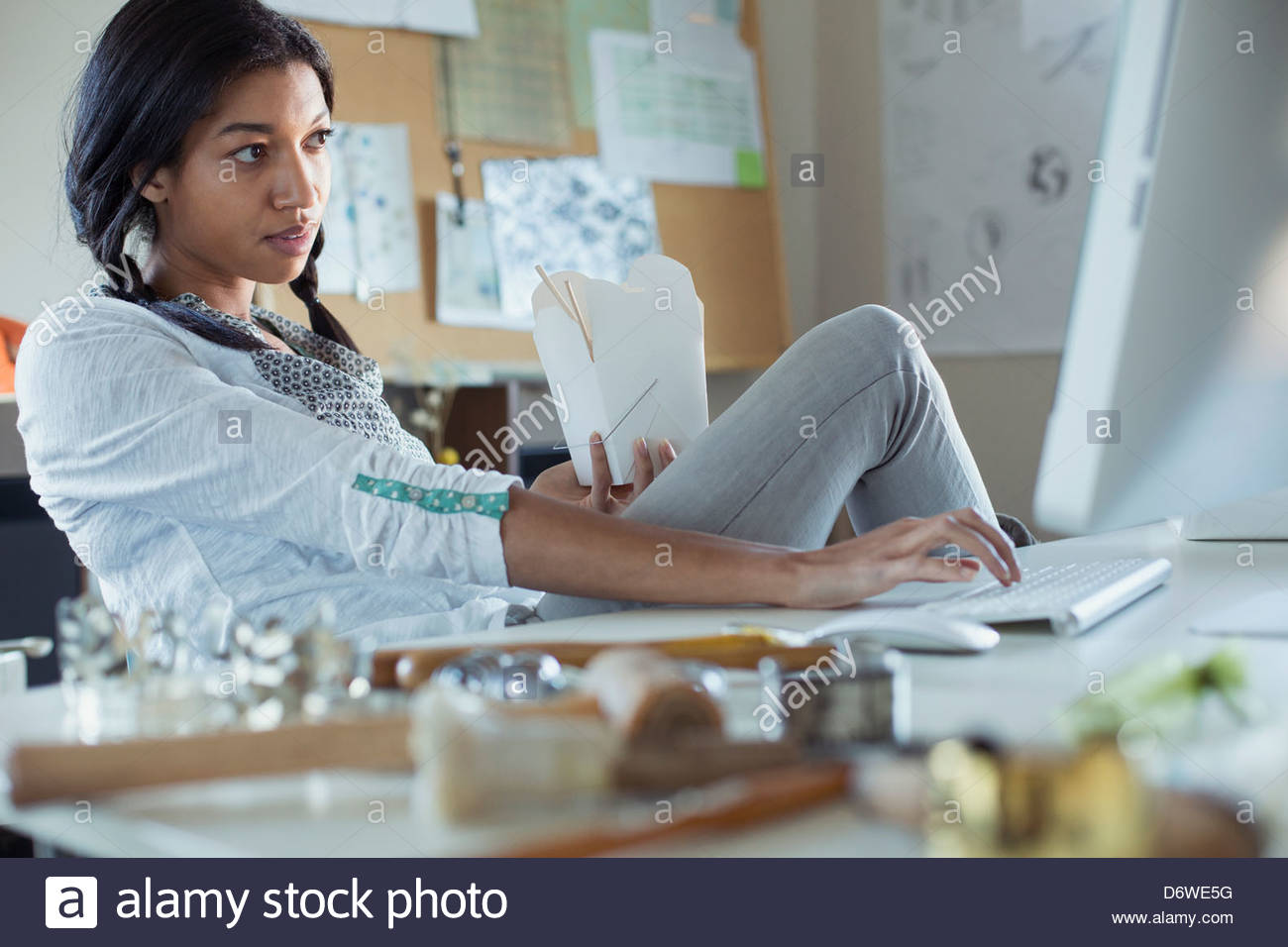 Female jewelry artist with take out food using computer at work Stock Photo
