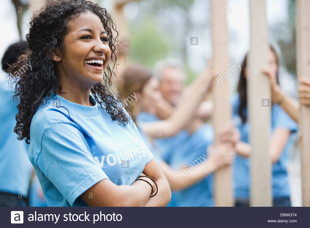 Cheerful teenage girl with volunteers building wooden frame in