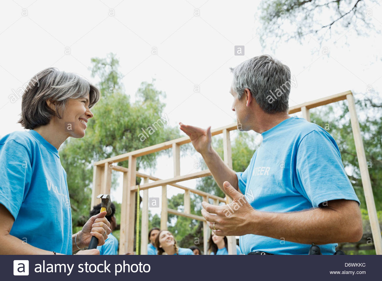 Mature man and woman talking while volunteers build wooden frame in background Stock Photo