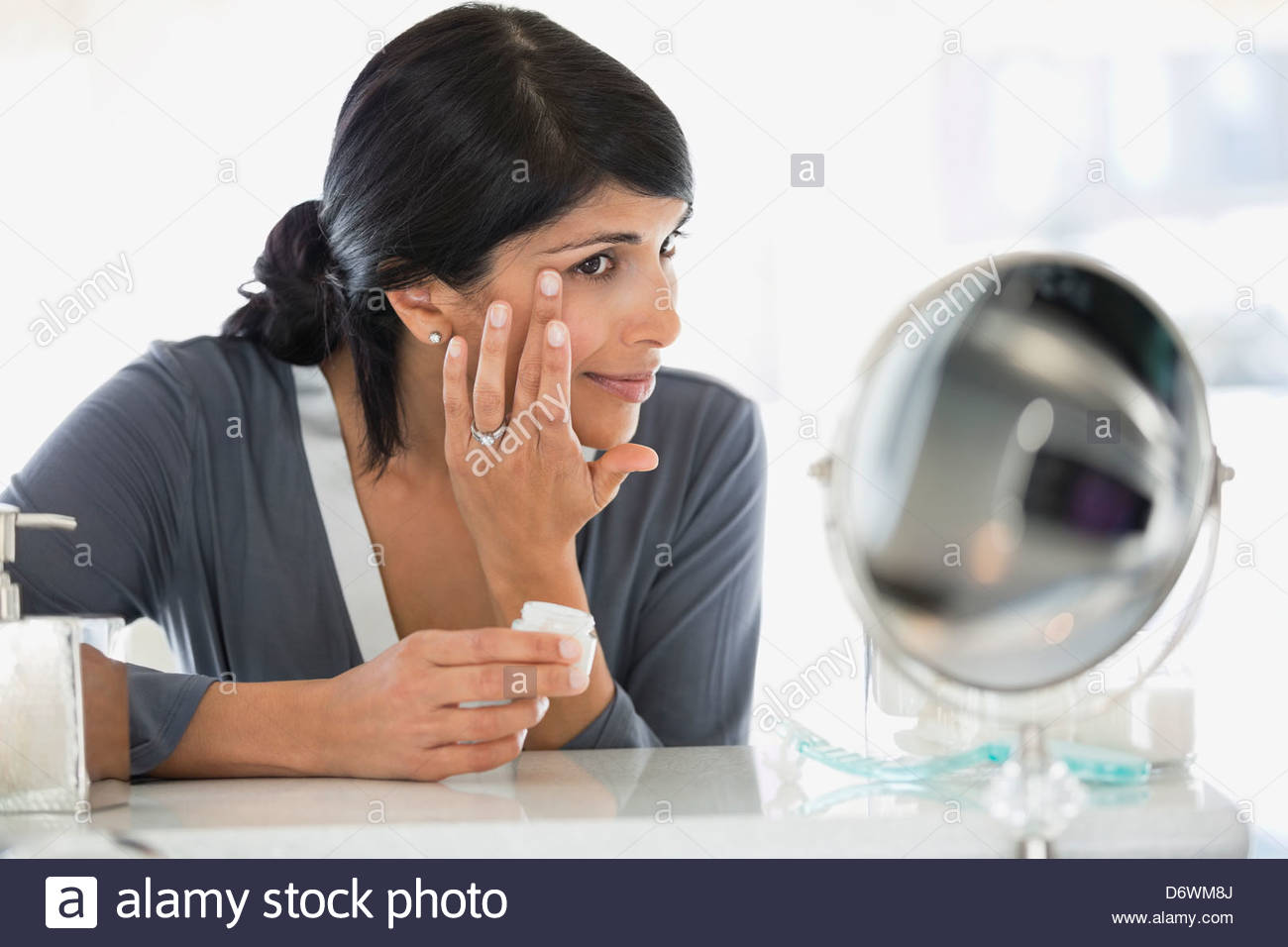 Beautiful mature woman applying cream on face at dressing table Stock Photo