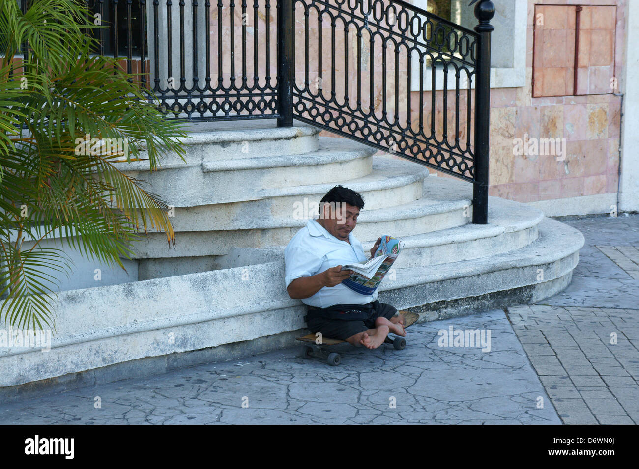 Handicapped man sitting on a skateboard and reading a newspaper, Cancun, Quintana Roo, Mexico Stock Photo