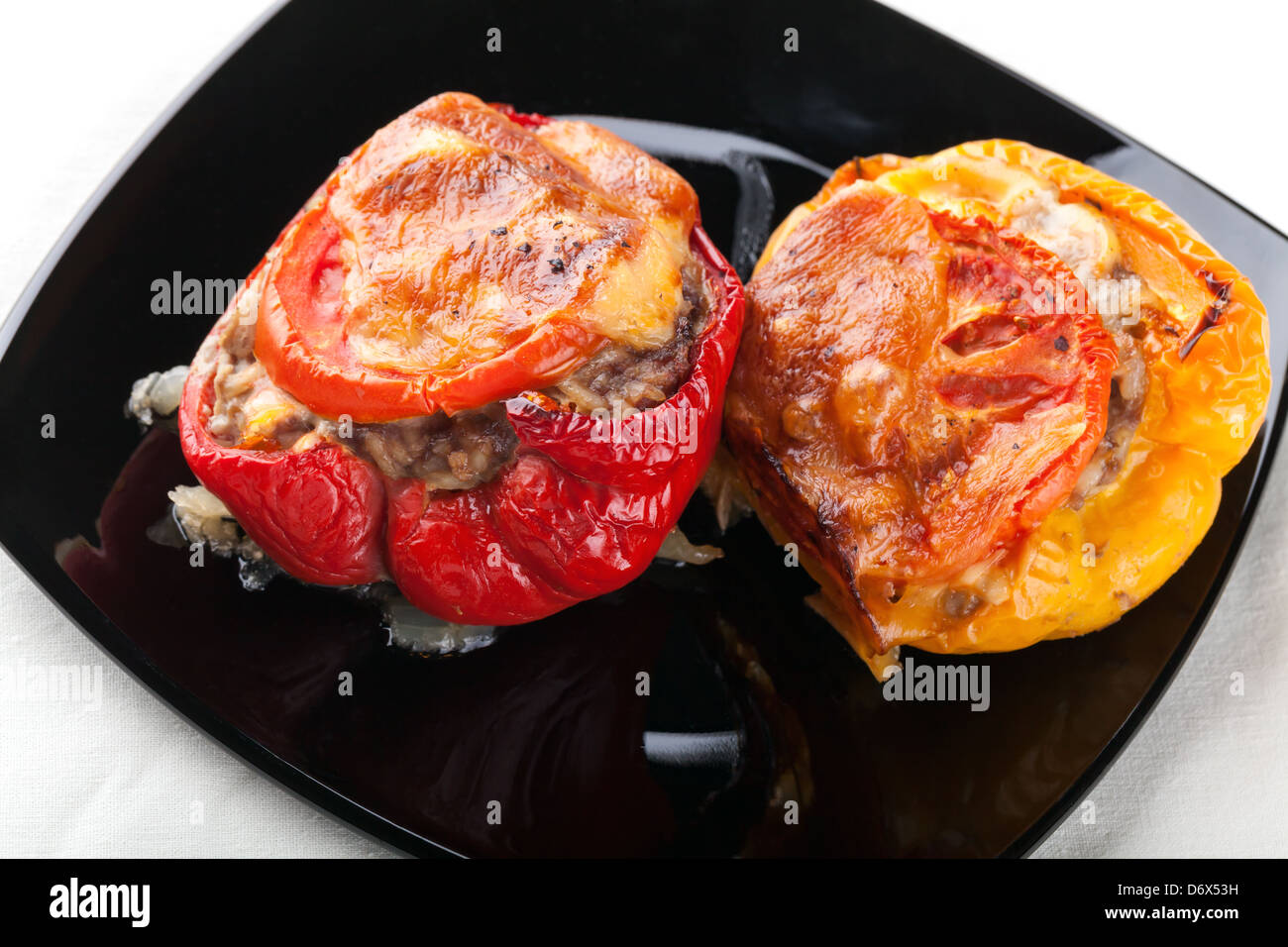 Two stuffed bell peppers with chopped meat, cheese and tomato on black plate Stock Photo