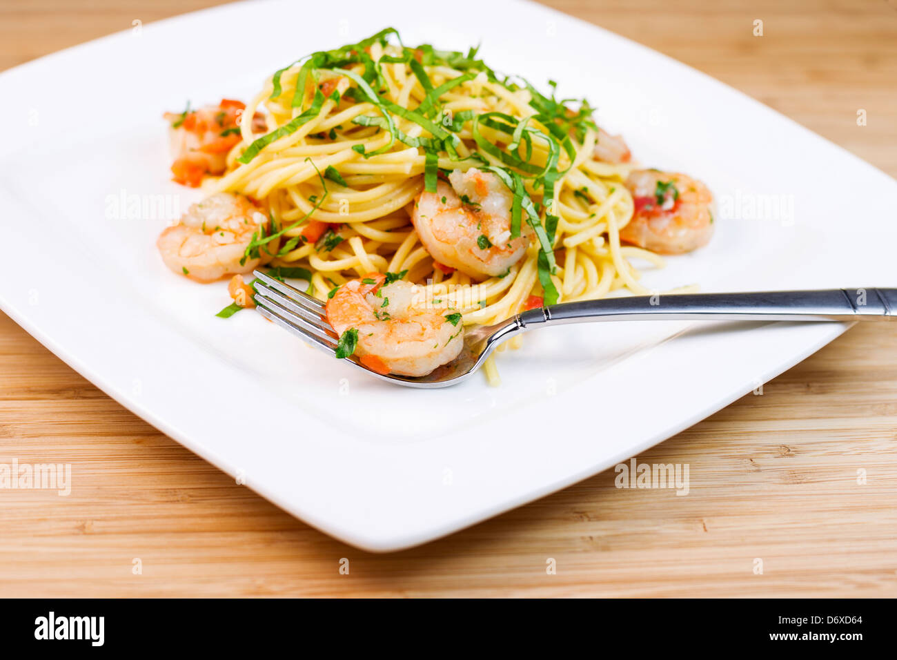 Closeup horizontal photo of Pasta dish with large shrimp, basil, parsley, stainless steel fork Stock Photo