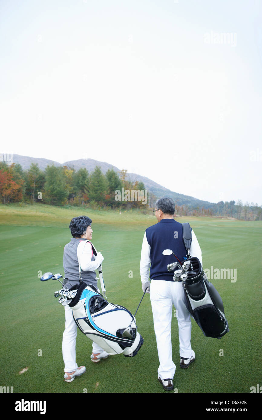 back shot of a couple with golf bags walking at a golf course Stock Photo