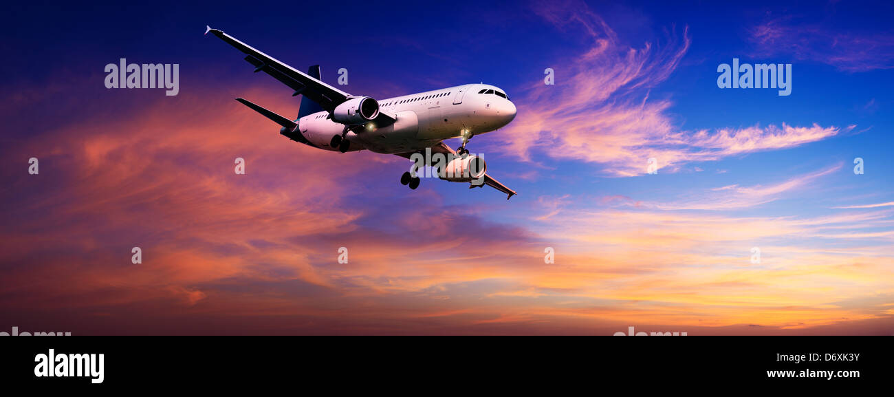 Jet is maneuvering for landing in a sunset sky. Panoramic composition. Stock Photo