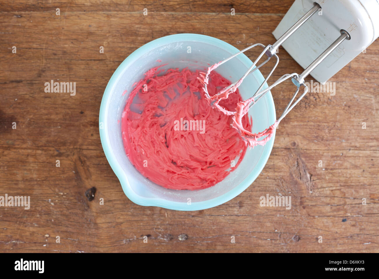 electric mixer with pinkish/red frosting on the beaters with a blue bowl, Stock Photo