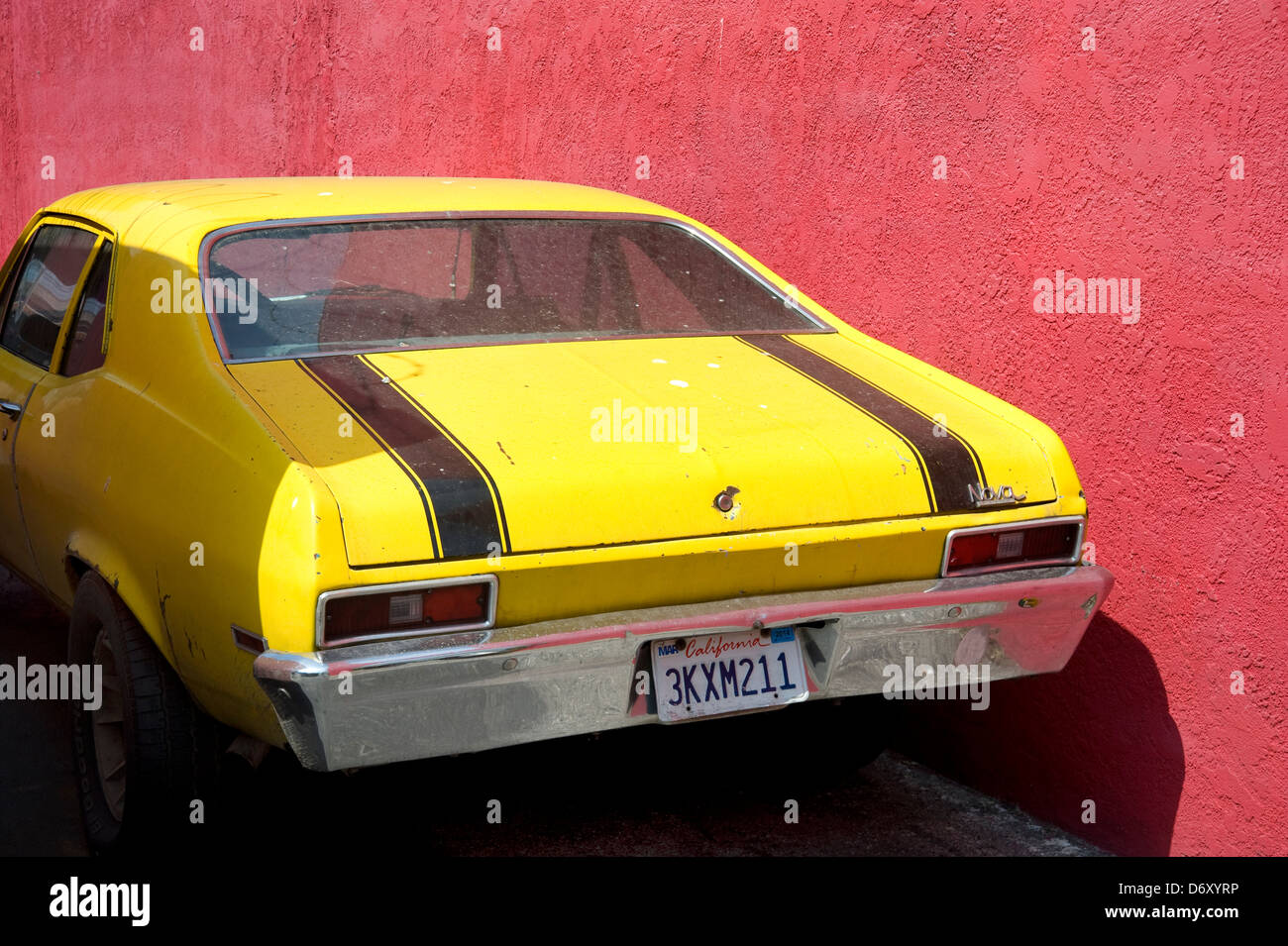 Bright yellow car parked against red wall Stock Photo