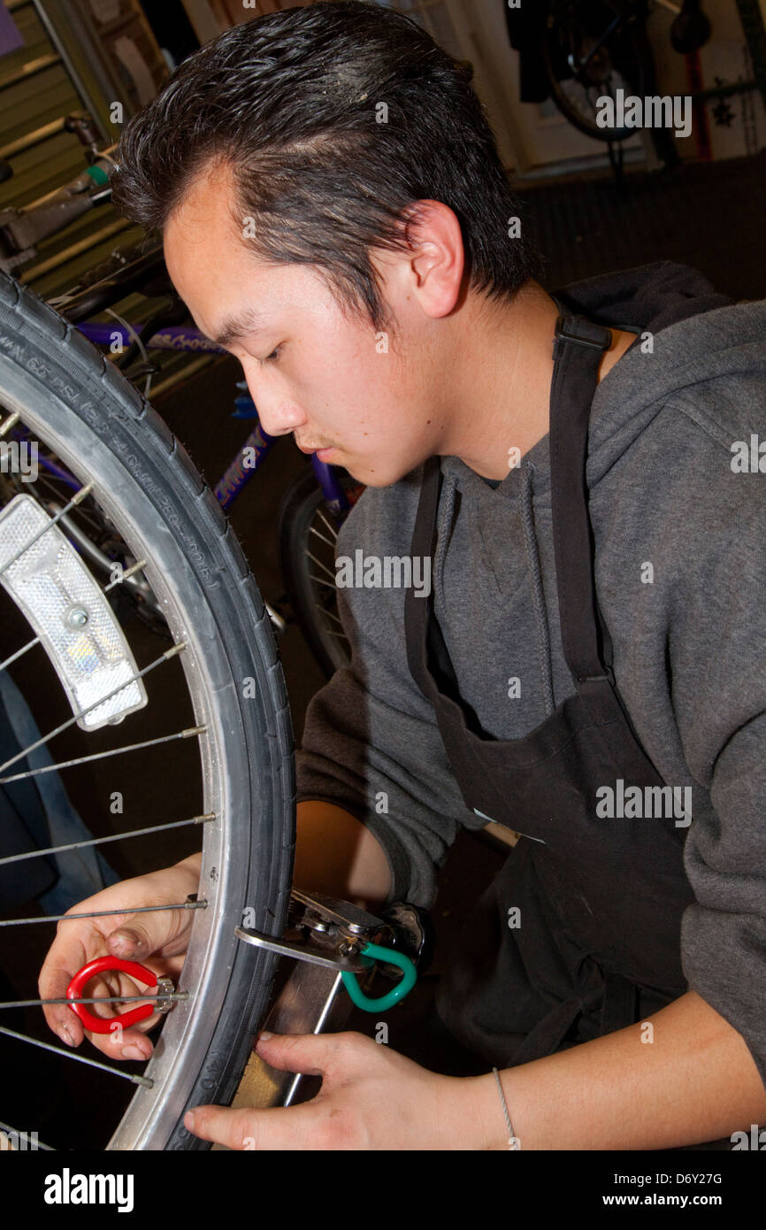 Asian teen adjusting bicycle spoke tension at the nonprofit Youth