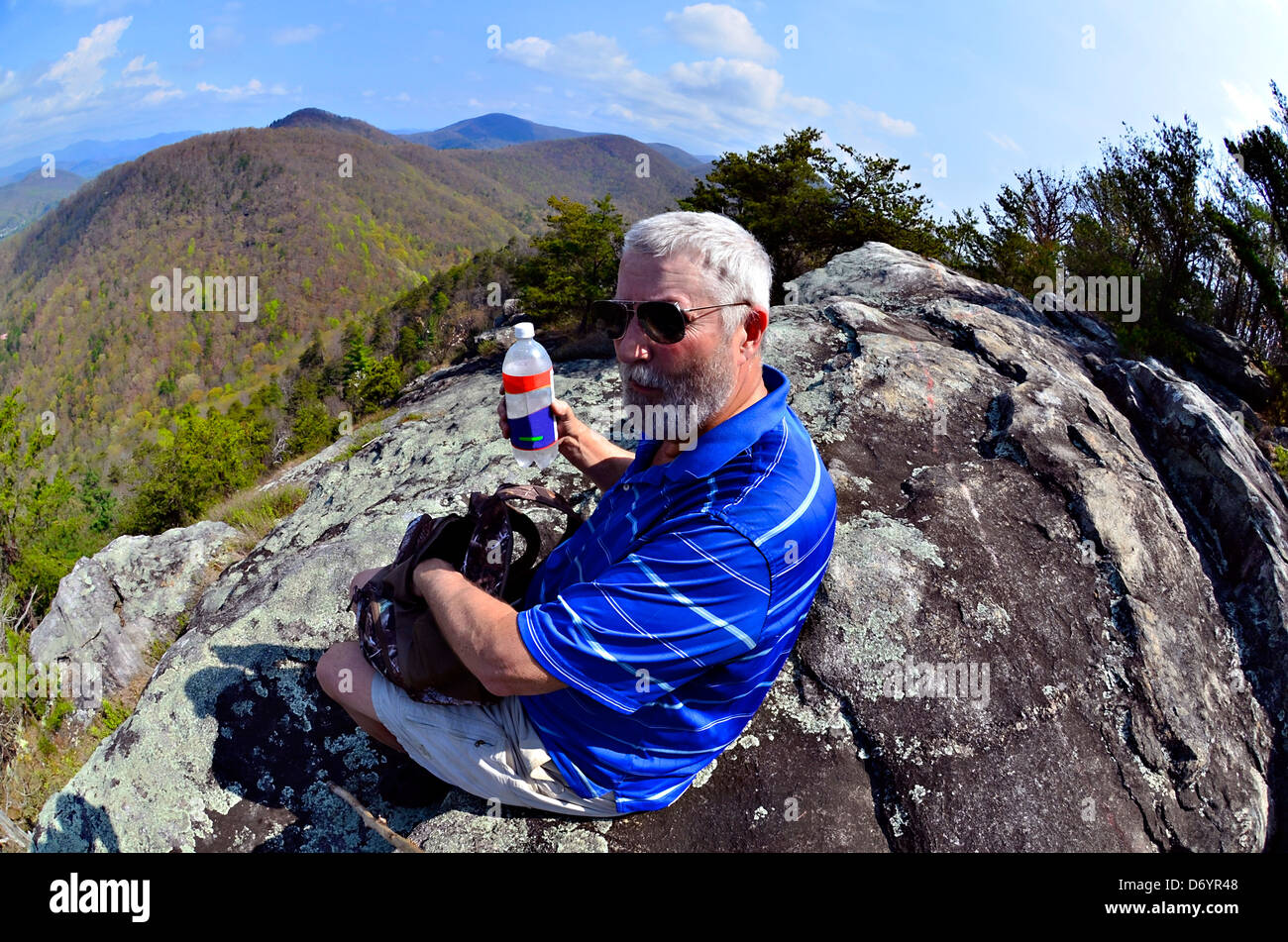 Older man on a rock overlook stopping to eat and drink in the Smoky Mountains. Taken with fisheye lens. Stock Photo