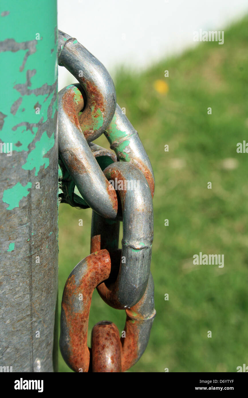 The rust covered links of a steel chain on a green fence in a park in Cotacachi, Ecuador Stock Photo