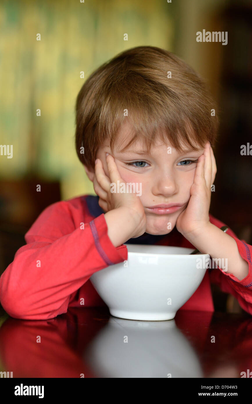 An unhappy boy aged five years old, with a bowl of cereal. Stock Photo