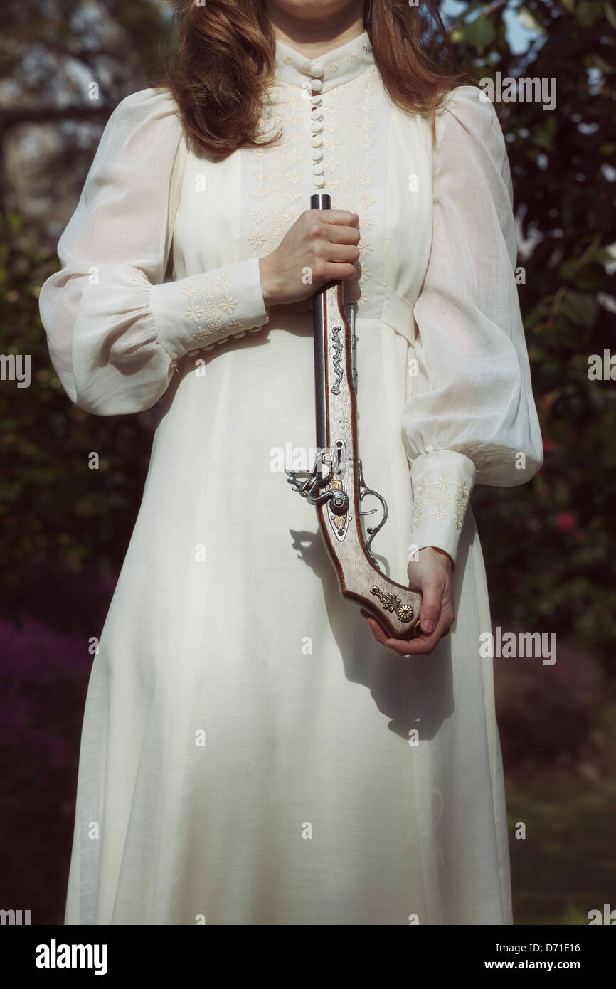 a woman in a vintage dress with an old rifle Stock Photo