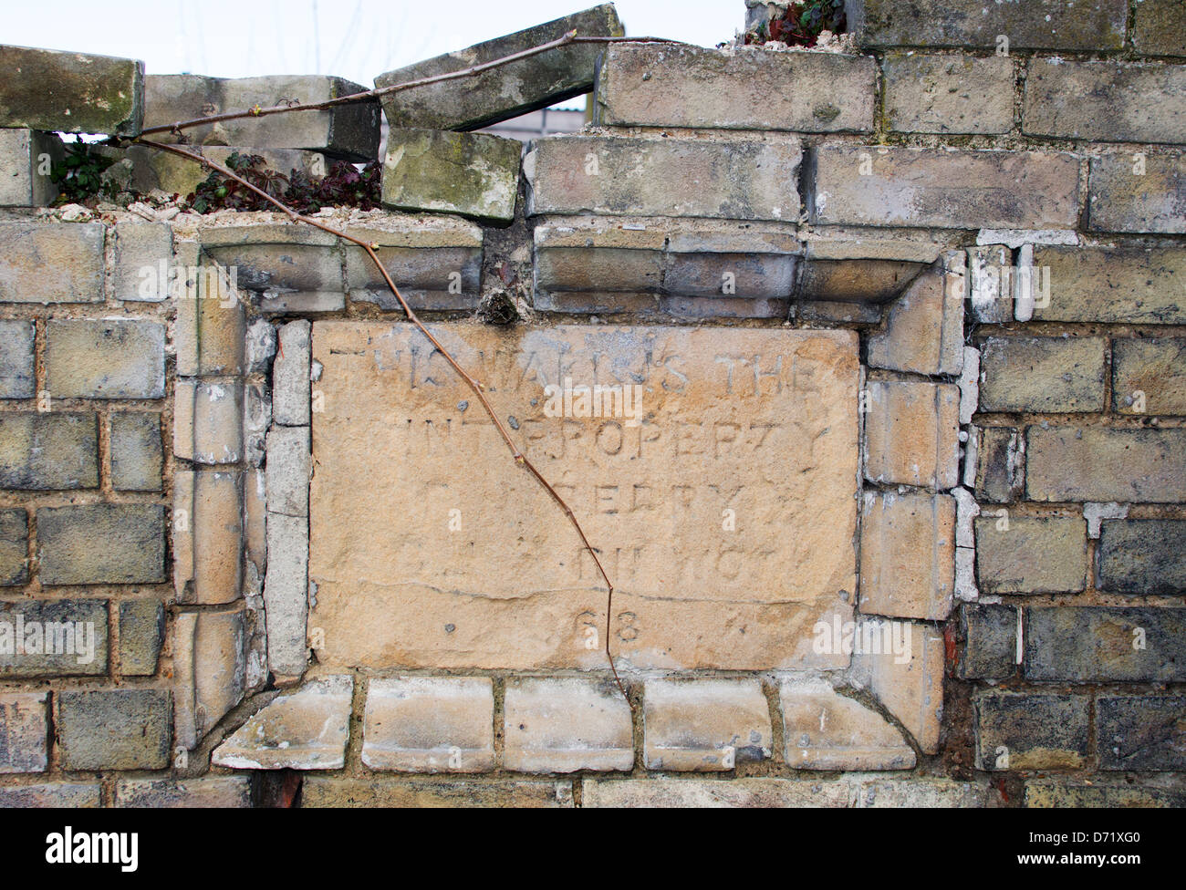 A stone tablet set in an old wall, marking the wall's ownership. The faded inscription suggests 19th Century. Stock Photo