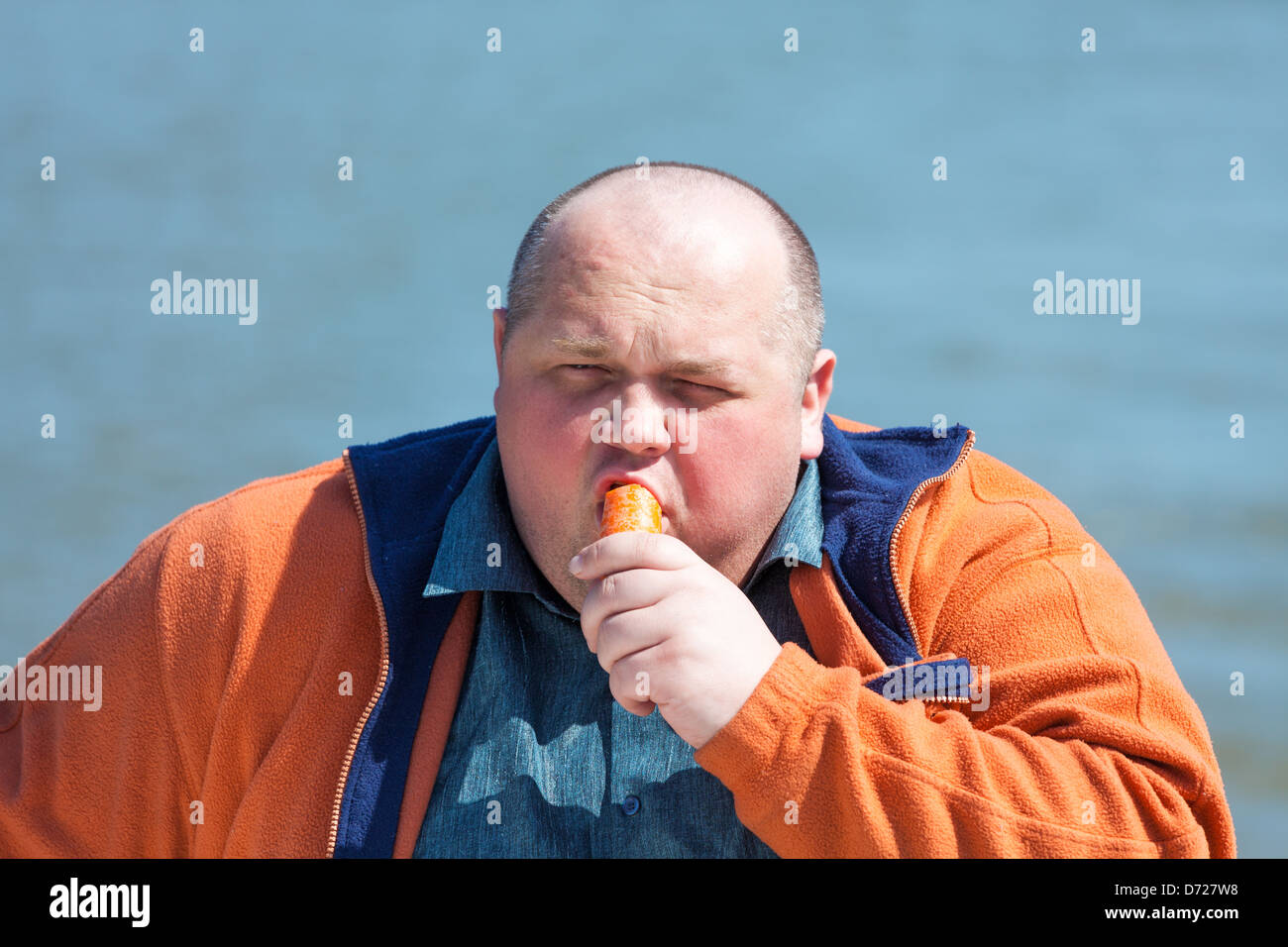 Fat man eating a carrot, on a background of water Stock Photo
