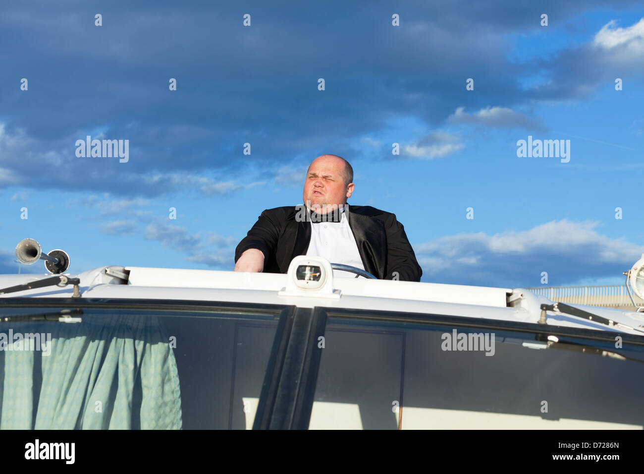 Overweight man in a tuxedo at the helm of a pleasure boat, closeup