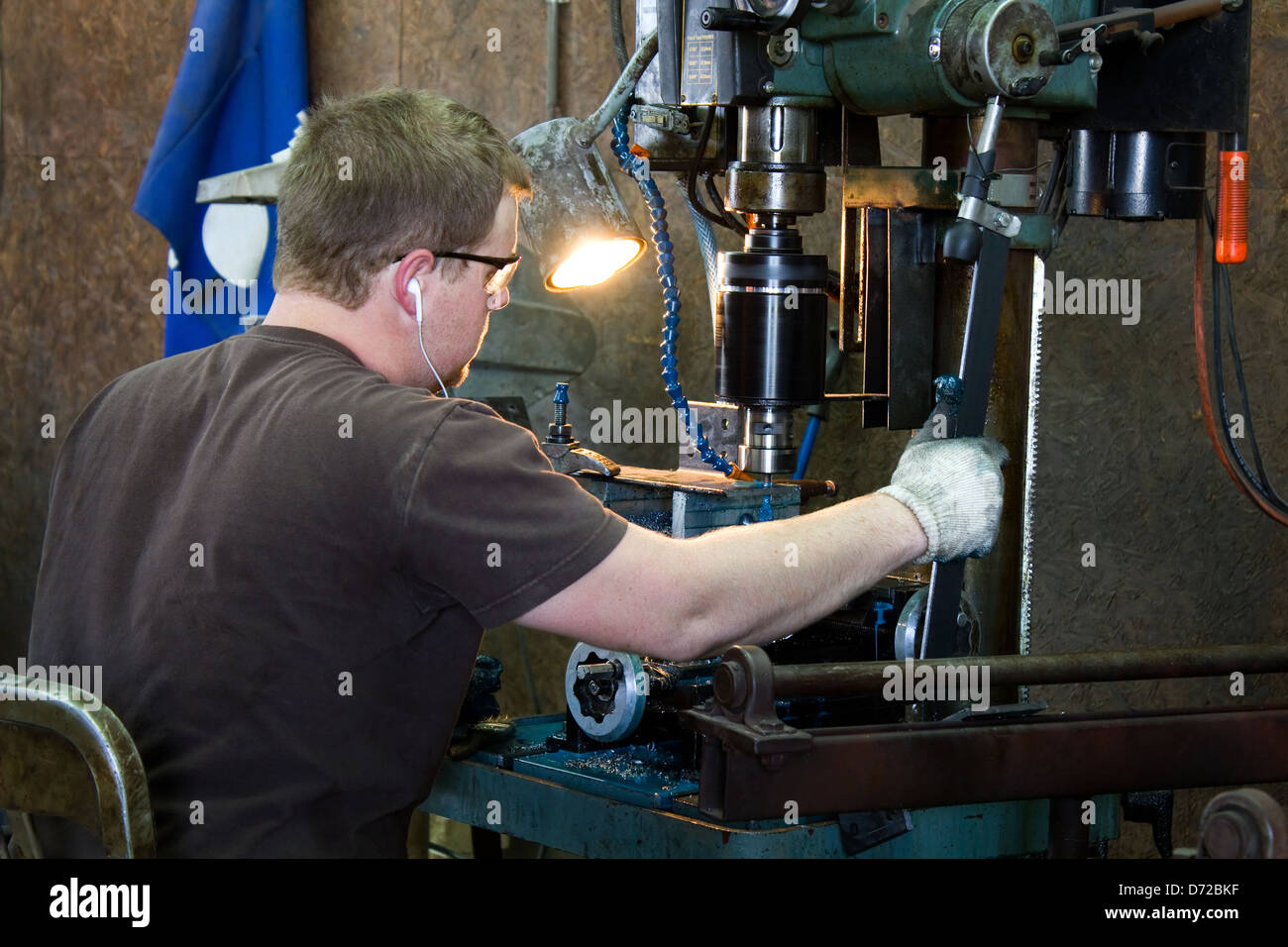 Machinist taps threads into steel using a drill press in production work in a metal shop. Stock Photo