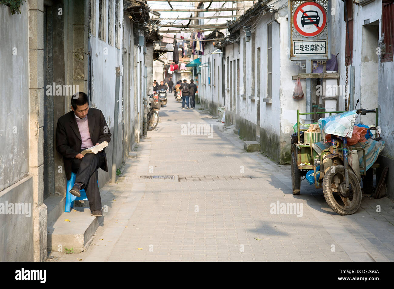 A local man reads on his doorstep on an old town street, Suzhou, China Stock Photo