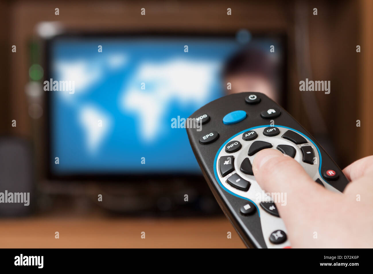 Hand holding TV remote control with a television in the background. Close up. Stock Photo