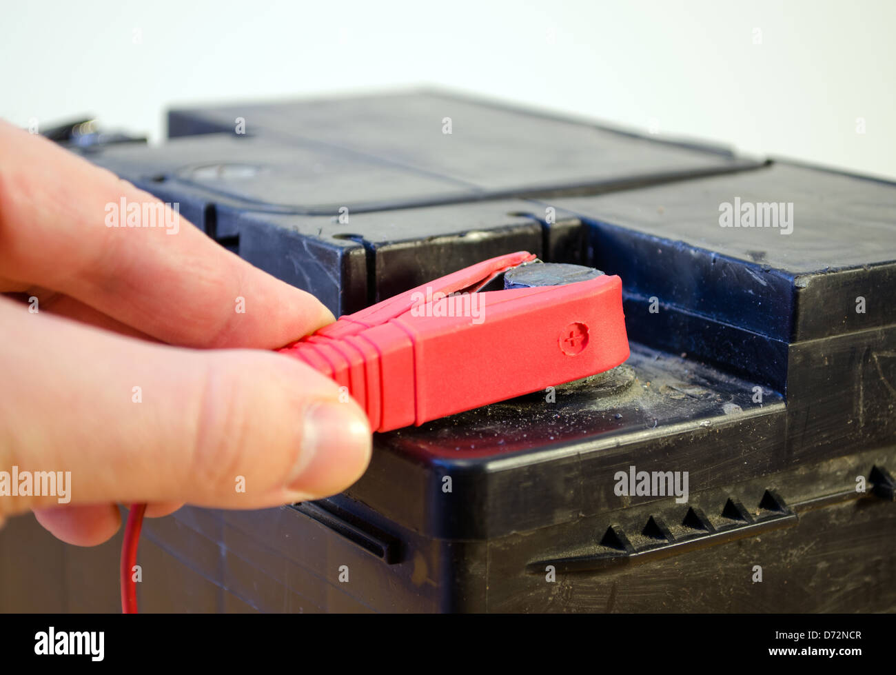 closeup of hand plug car automobile battery charger red clamp on accumulator plus. Stock Photo