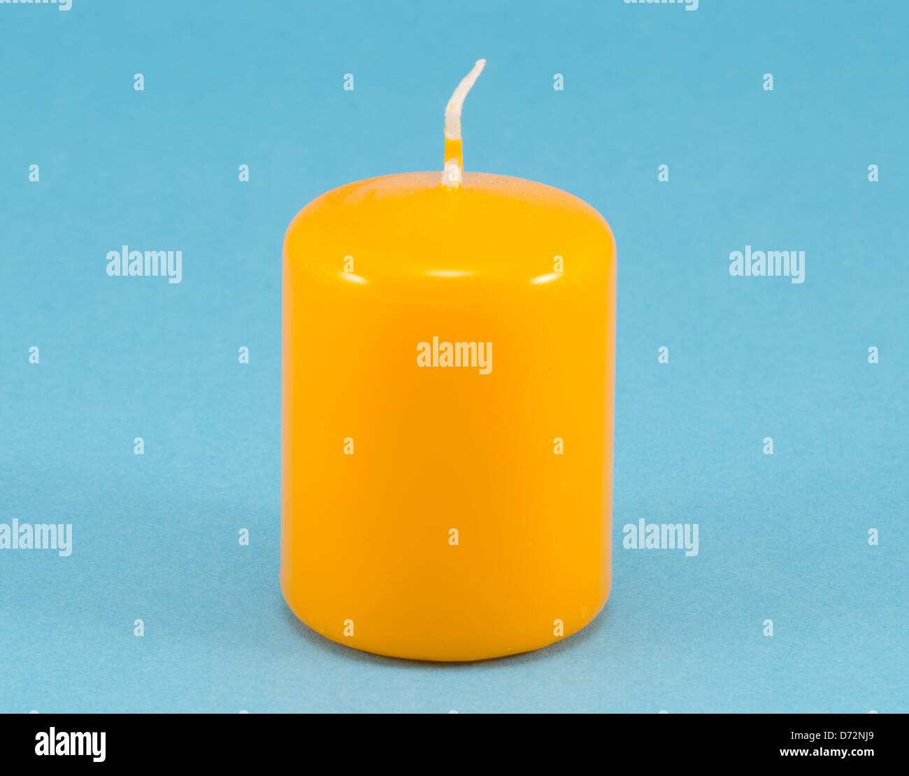 yellow thick simple wax candle with wick on blue background Stock Photo
